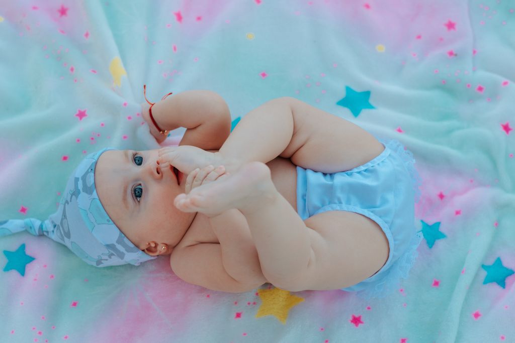 Cute baby in a blue outfit playing on a colorful star-patterned blanket.